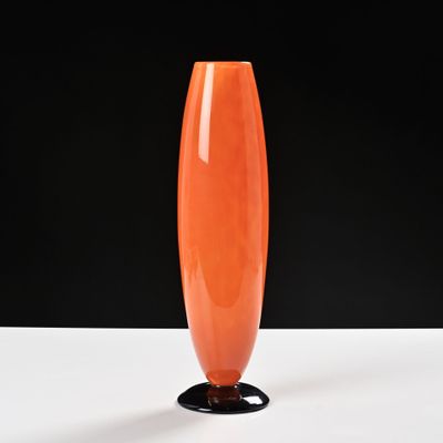 un vase orange posé sur une table blanche