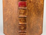 an old book with a red cover sitting on top of a table