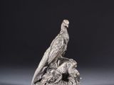 an antique silver figurine of a bird on a rock