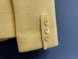 une veste jaune en tricot avec des boutons, suspendue à un cintre devant un mur bleu