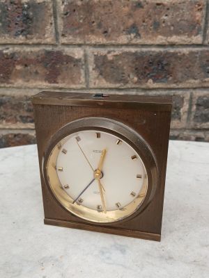 une petite horloge posée sur une table, avec un mur de briques en arrière-plan