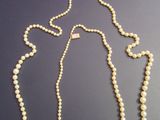 a white pearl necklace with a gold clasp on a black surface