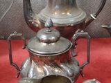 une théière en argent et deux tasses en argent posées sur une nappe rouge