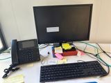 a desk with a computer, telephone, and other items on it