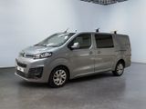 La camionnette argentée est garée dans une grande pièce aux murs blancs.