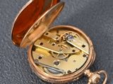 a gold pocket watch with a red dial on it