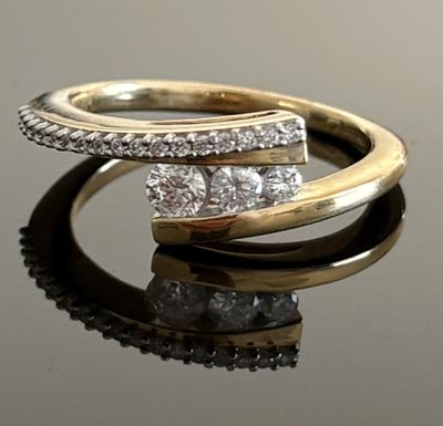 un gros plan d'une bague en or et diamants posée sur une surface réfléchissante