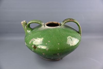 un vase vert posé sur une table, sur fond blanc