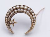 a close up of a crescent shaped brooch with pearls and a star