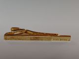 an image of a gold tie bar sitting on top of a white table