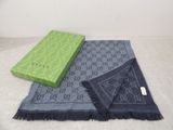 Une écharpe et un coffret Guccissi posés sur un lit, avec un mur blanc en arrière-plan