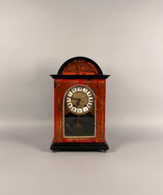 une petite horloge rouge avec un cadran doré sur fond blanc