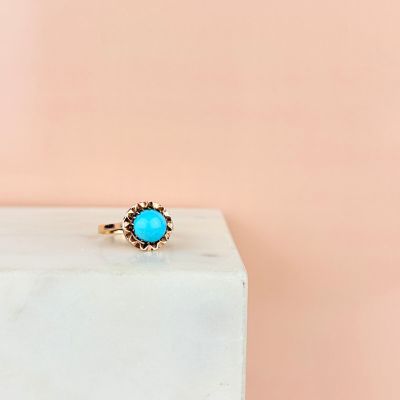 a gold ring with a turquoise stone sits on a marble block