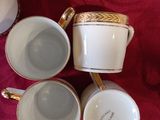 three white and gold coffee cups sitting on top of a red table cloth