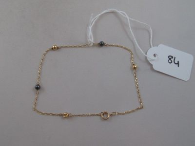 gold plated ankle chain with black beads and a white tag