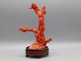 une sculpture orange représentant une femme tenant un oiseau, posée sur un socle en bois