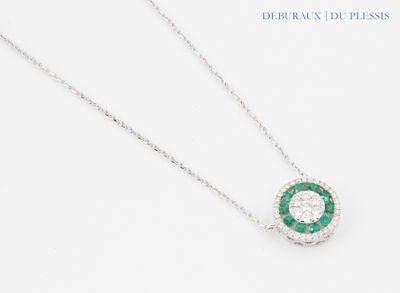 un gros plan d'un collier de diamants et d'émeraudes posé sur une surface blanche