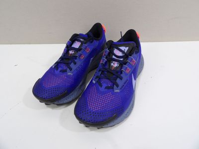 une paire de chaussures de course violettes et noires posées sur une surface blanche