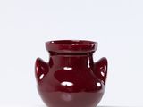 un petit vase rouge posé sur une surface blanche