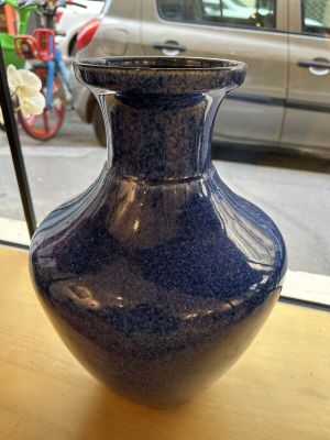 un vase bleu posé sur une table devant une fenêtre