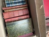 un homme tenant une boîte remplie de livres devant une pile de livres