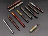 six stylos différents et une chaîne posés sur une surface noire