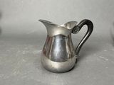 a silver pitcher sitting on a table next to a cup