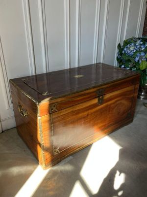 a wooden trunk sitting on the floor next to a vase of flowers
