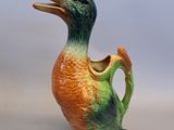 un vase en forme de canard, de couleur orange et verte, posé sur une table