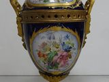 a gold and blue vase on a stand with flowers on it