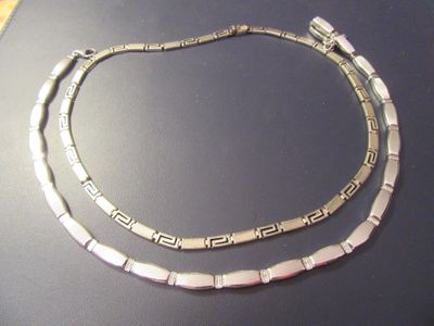 two silver necklaces on display on a table with a black background