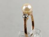 gold ring with a pearl and diamonds on top of a clear glass