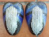 two blue vases with white feathers on them sitting on a tile floor