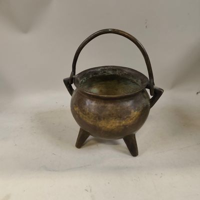 une vieille casserole en laiton avec une poignée, posée sur une surface blanche
