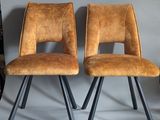 pair of brown leather chairs with metal legs against a gray wall