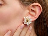 La femme porte une paire de boucles d'oreilles ornées de fleurs.