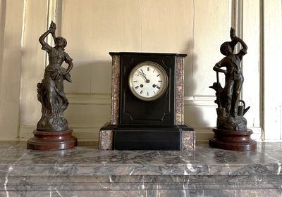 trois statues et une horloge posées sur une table en marbre