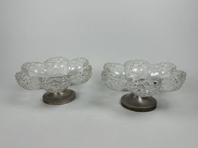 une paire de bols en verre transparent posés sur des socles métalliques, sur fond blanc