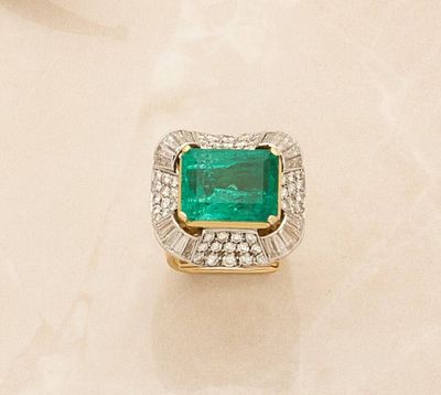 an emerald and diamond ring on a white marble surface