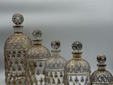 cinq bocaux en verre ornés de motifs dorés sont alignés sur une surface blanche