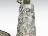 a glass bottle with a silver lid next to a metal container