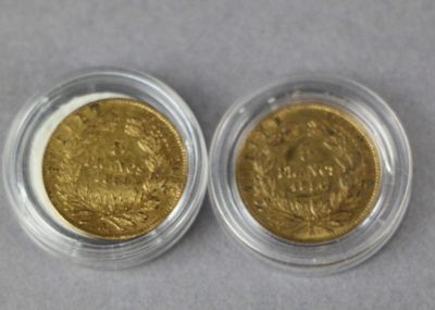 two gold coins in a clear plastic container on a gray surface