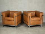 two brown leather chairs sitting next to each other on a cement floor