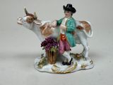 une figurine représentant un homme chevauchant une vache, avec un panier de fleurs