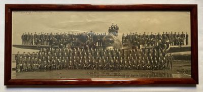 une vieille photo montrant un groupe d'hommes debout devant un avion