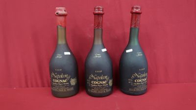 trois bouteilles de vin sont alignées sur une surface rouge