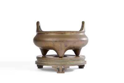 un petit pot en bronze posé sur un socle, sur une surface blanche
