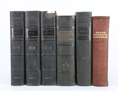 Plusieurs livres anciens sont alignés sur une étagère devant un fond blanc