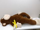 a stuffed monkey laying on a table with a banana in it ' s mouth