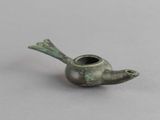 une vieille pipe en bronze en forme d'oiseau posée sur une surface grise